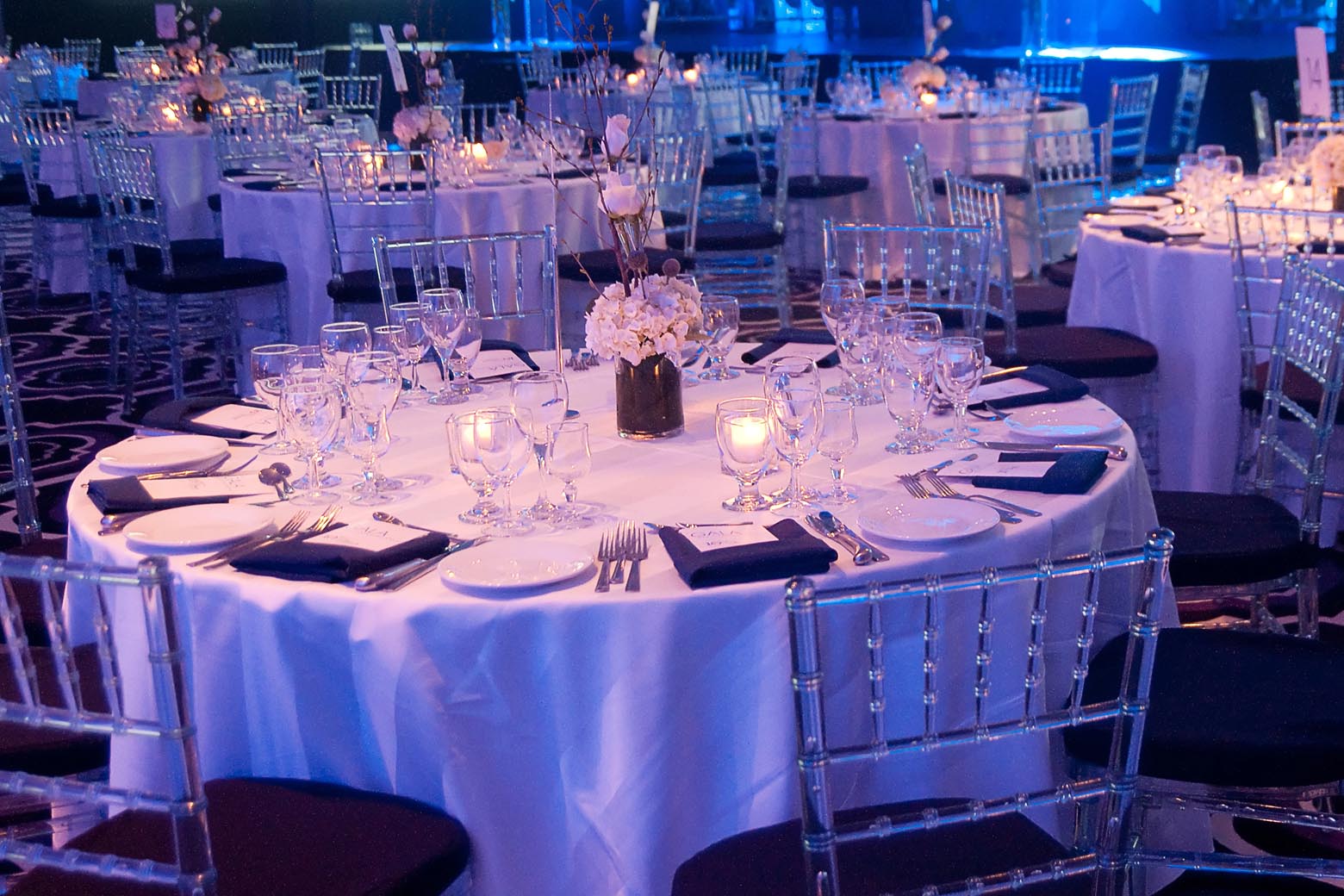 Round banquet tables illuminated with blue light and candles.