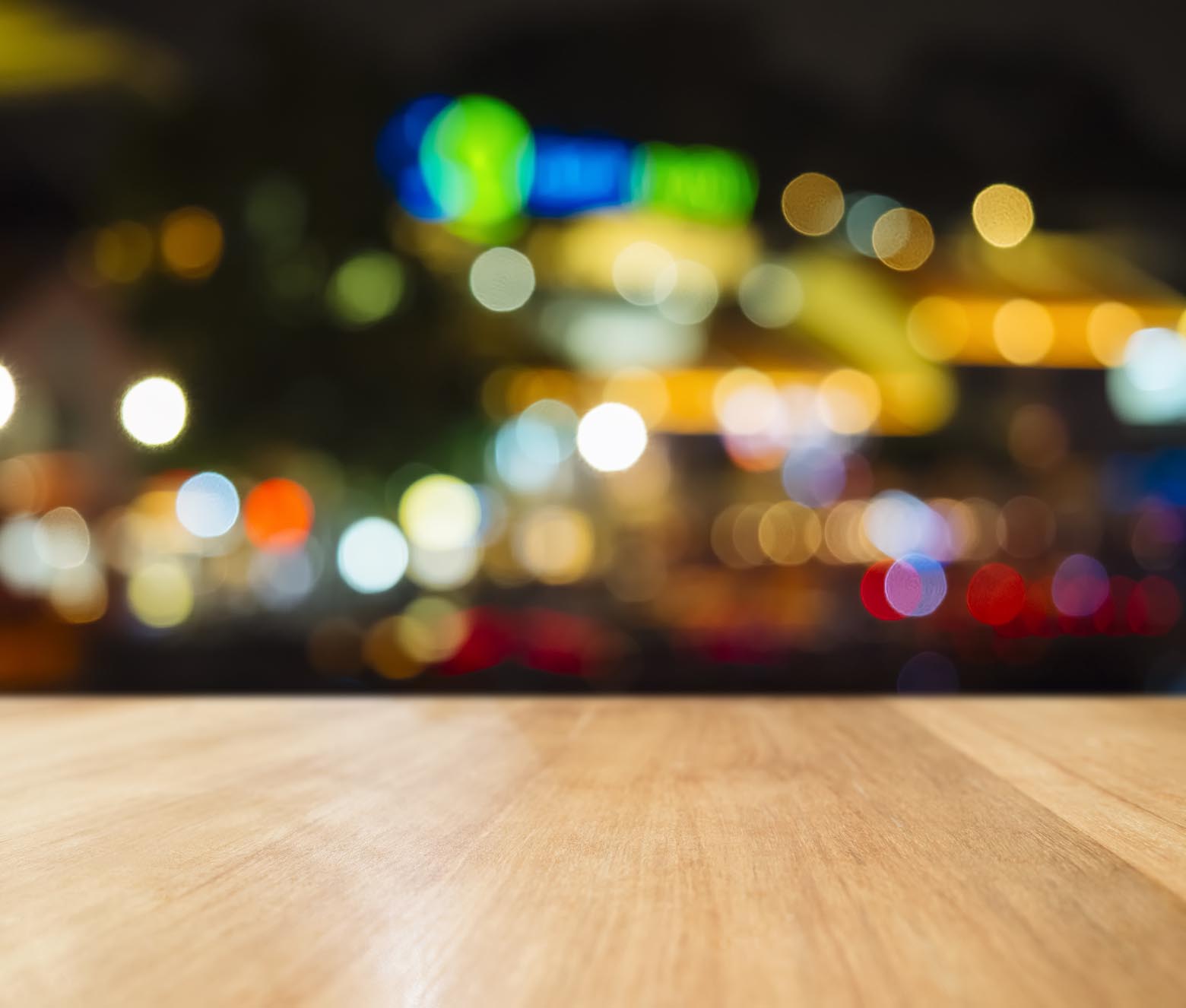Empty wooden tabletop against colorful blurred city lights.
