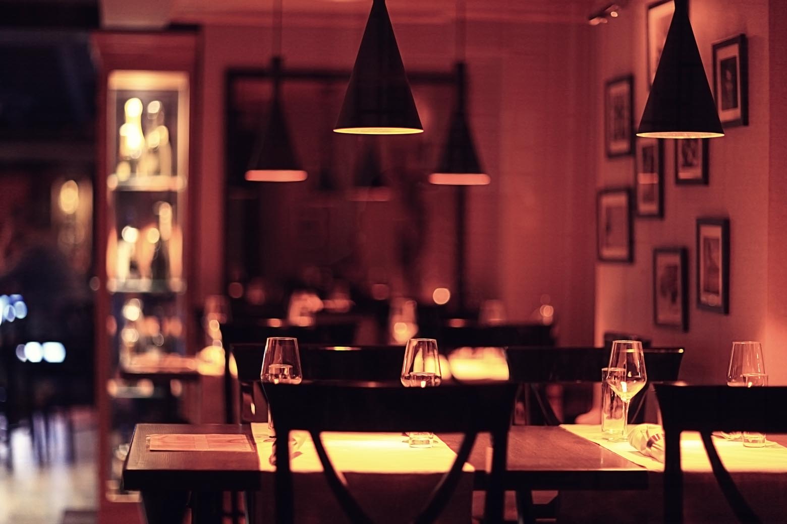 Warmly lit restaurant tables beneath black pendant lamps.
