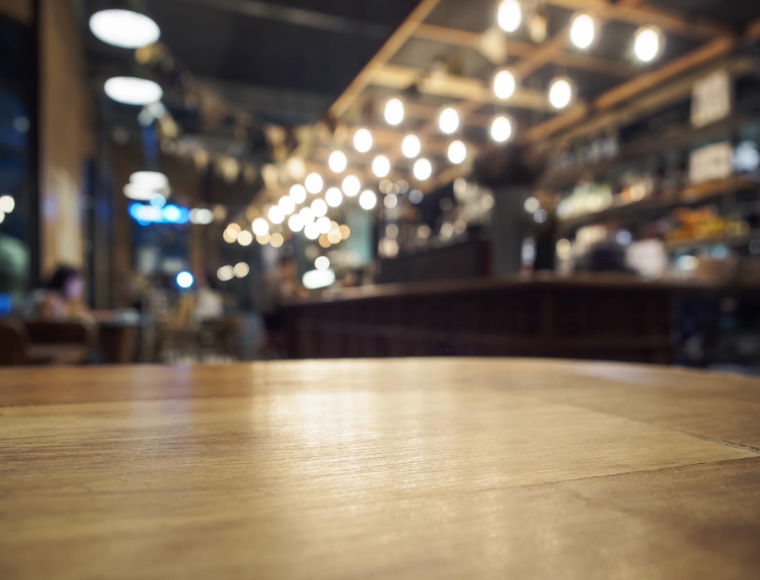 Empty wooden bar counter beneath rows of glowing lights.
