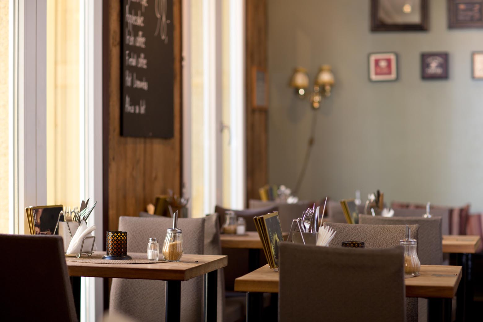 Sunlit restaurant interior with wooden tables and upholstered chairs.