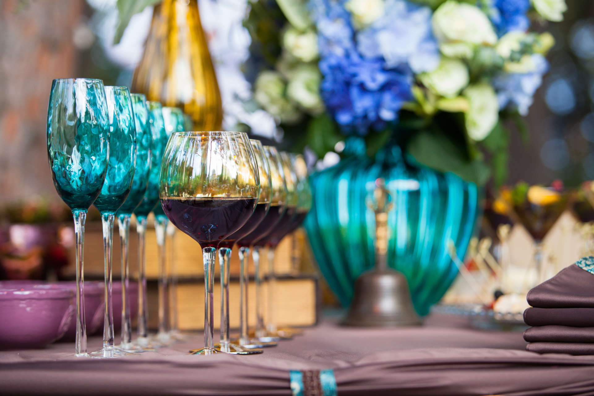Turquoise glasses, red wine, and blue hydrangeas arranged on an event table.